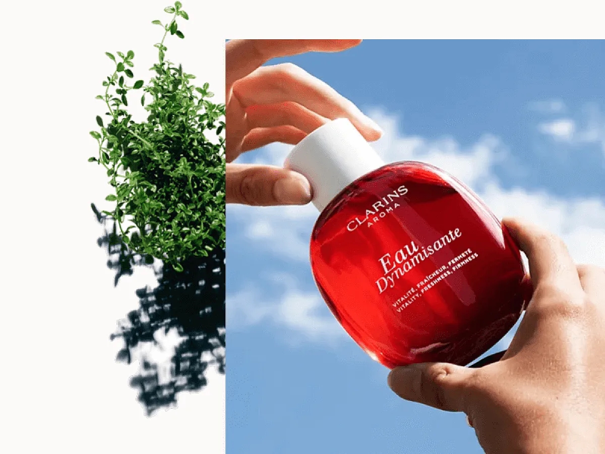 70 Jahre Clarins: Hände halten das Eau Dynamisant von Clarins vor einen strahlend blauen Himmel